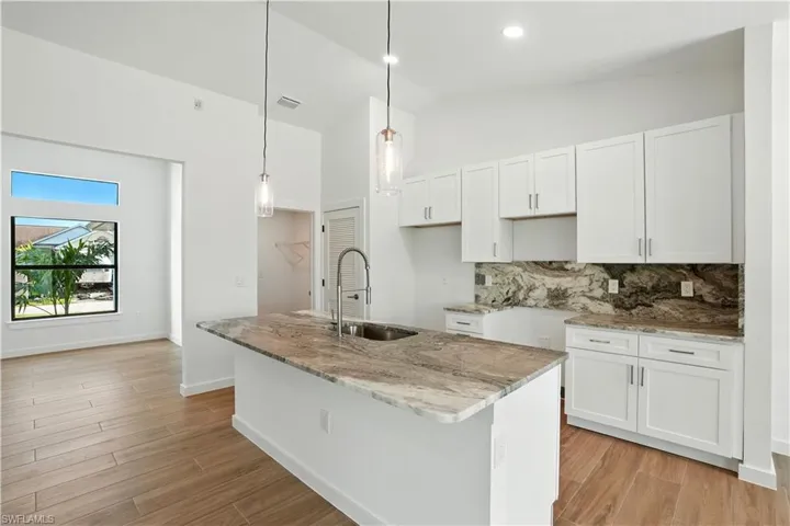 Kitchen with light stone countertops, white cabinetry, tasteful backsplash, light wood-style floors, and vaulted ceiling