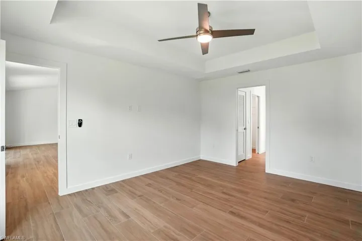 Empty room with a tray ceiling, ceiling fan, and light wood finished floors