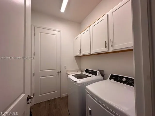 Washroom featuring dark wood-type flooring, washing machine and clothes dryer, and cabinets