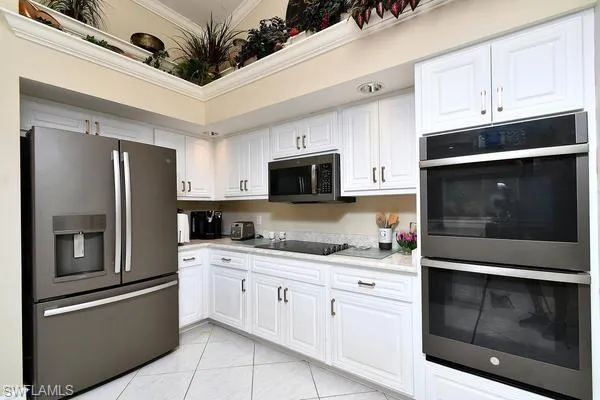 Kitchen with stainless steel appliances, white cabinets, light tile patterned flooring, and ornamental molding