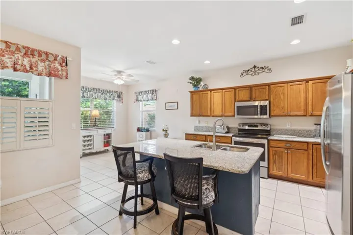 Kitchen featuring light stone countertops, a kitchen bar, a kitchen island with sink, light tile patterned floors, and appliances with stainless steel finishes