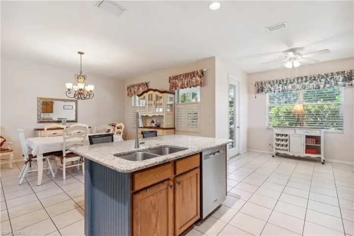 Kitchen featuring stainless steel dishwasher, sink, light tile patterned floors, and a kitchen island with sink