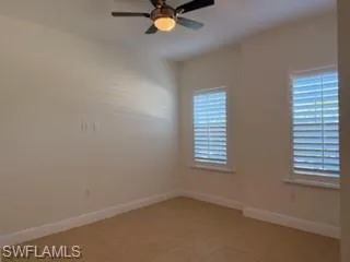 Room featuring two windows with white plantation shutters, a ceiling fan with integrated lighting, and tile flooring