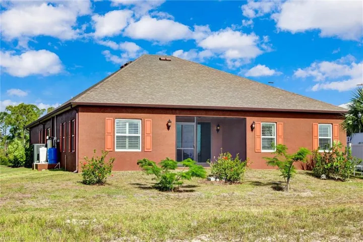 Rear exterior featuring a screened lanai, textured siding, contrasting window shutters, and a shingled roof