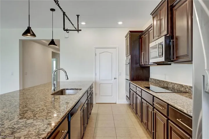 Kitchen featuring a large island with an undermount sink, dark wood cabinetry, granite countertops with a matching backsplash, and recessed lighting