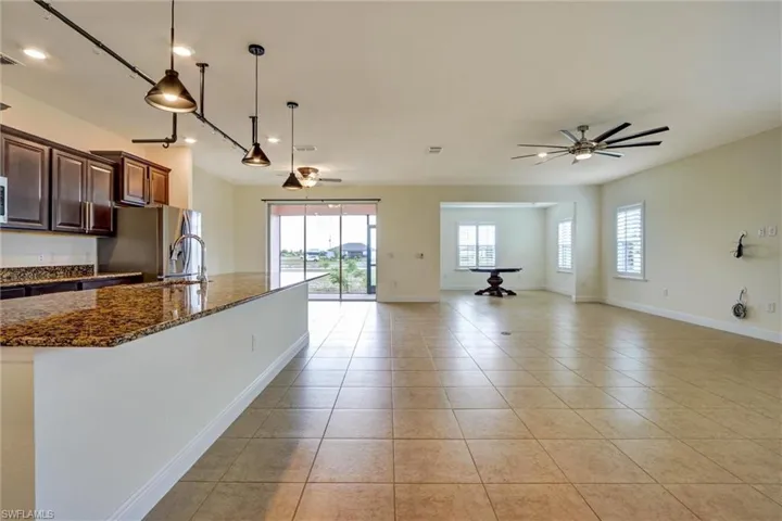 Open-concept living space featuring tile flooring, a kitchen island with granite countertops, dark wood cabinetry, and stainless steel appliances