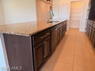 Kitchen island featuring a granite countertop, undermount sink with gooseneck faucet, dark wood cabinetry, and stainless steel dishwasher