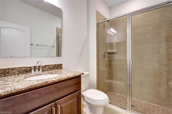 Bathroom featuring a glass-enclosed shower with tile surround, a dark wood-finish vanity with a stone countertop, an undermount sink, and chrome fixtures
