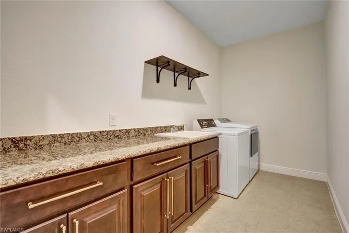 Laundry room featuring dark wood-finish cabinetry with golden hardware, a light-toned countertop, and a built-in sink