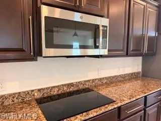 Kitchen featuring rich wood-finish cabinetry, a stainless steel over-the-range microwave, and a black glass cooktop integrated into a speckled countertop