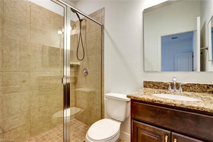 Bathroom featuring a glass-enclosed shower with full-height tile surround, a built-in shower bench, and a vanity with a granite-look countertop and under-mount sink