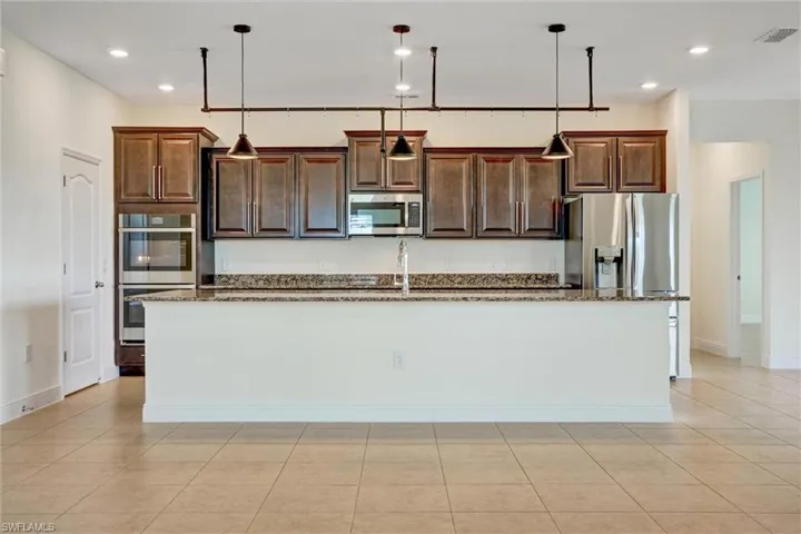 Open-concept kitchen featuring an expansive island, dark wood cabinetry, stainless steel appliances, recessed lighting, and tile flooring