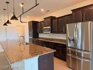 Kitchen featuring a large central island with a built-in sink and stone-finish countertop, dark wood-finish cabinetry, stainless steel appliances, and recessed lighting with pendant fixtures