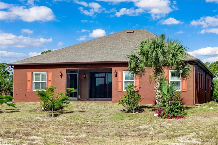 Rear exterior featuring a covered patio, multiple windows with decorative shutters, a shingle roof, and a palm tree