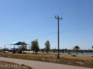Paved pathway bordering a recreational area featuring a covered playground and a lake