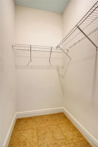 Walk-in closet featuring L-shaped wire shelving, textured white walls, and a light blue ceiling