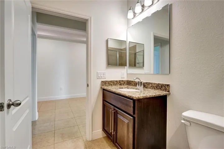 Bathroom featuring a single vanity with dark wood cabinetry, a light-toned stone countertop, a white undermount sink, and a chrome faucet