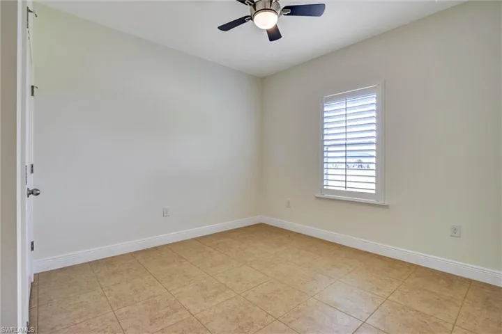 Bright room featuring a ceiling fan with light fixture, tile flooring, window with white plantation shutters, and white baseboards