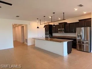 Open-concept kitchen featuring dark wood cabinetry, stainless steel appliances, a center island with bar seating, pendant lighting, and recessed ceiling lights