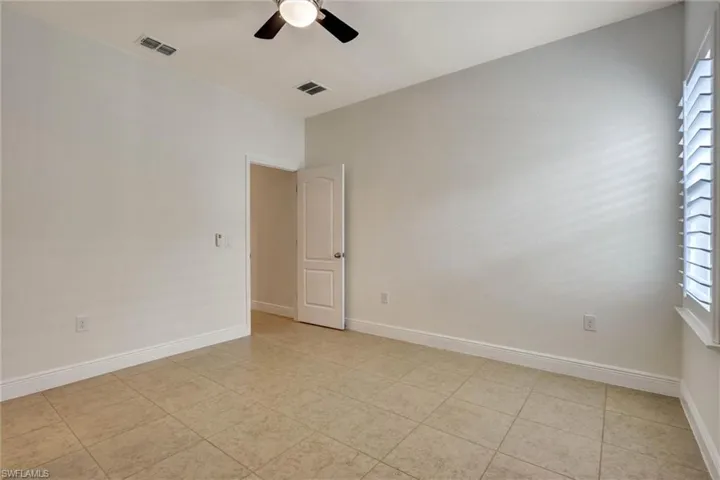 Spacious room featuring tile flooring, neutral wall tones, white trim, a ceiling fan, and window shutters