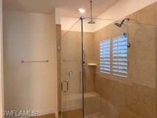 Walk-in shower featuring a glass enclosure, dual shower heads, integrated bench seating, and an accent window with plantation shutters
