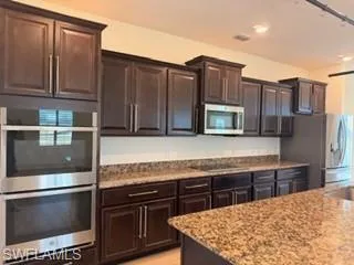 Kitchen featuring dark wood cabinetry with stainless steel hardware, a double wall oven, an over-the-range microwave, and a side-by-side refrigerator