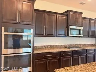 Rich wood-finish cabinetry complemented by stainless steel appliances, granite countertops, and a full-height backsplash