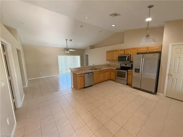 Kitchen with stainless steel appliances, a peninsula, light tile patterned flooring, hanging light fixtures, and open floor plan