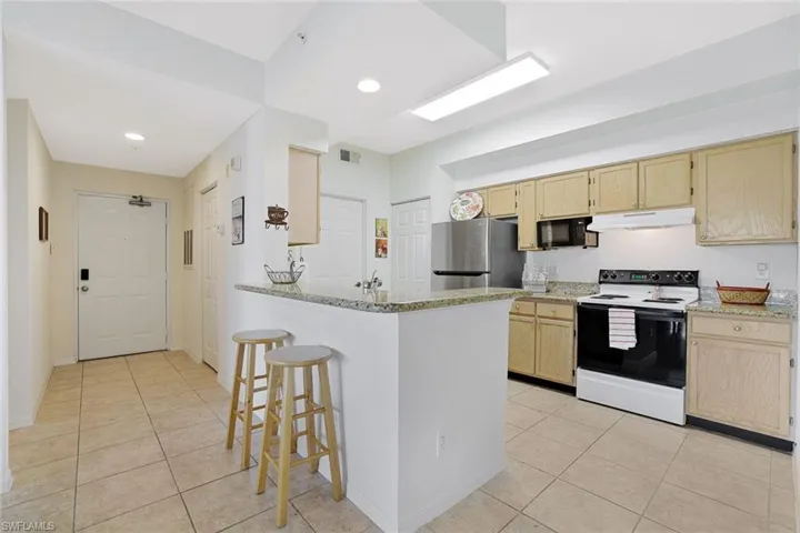 Kitchen featuring light brown cabinetry, a kitchen bar, range with electric stovetop, a peninsula, and recessed lighting