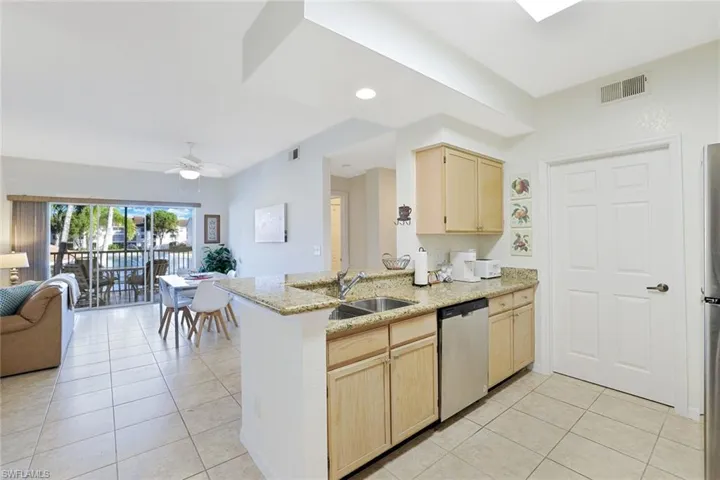 Kitchen with light brown cabinets, open floor plan, light tile patterned floors, light stone countertops, and stainless steel appliances