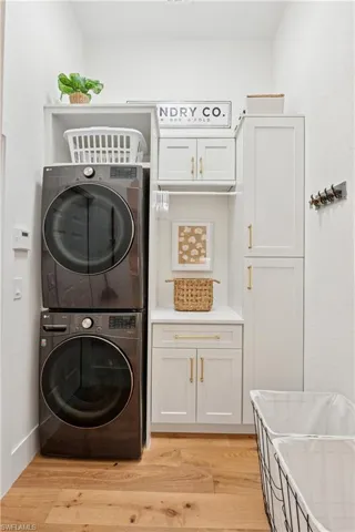 Laundry area featuring stacked washer / drying machine, cabinet space, and light wood-style floors