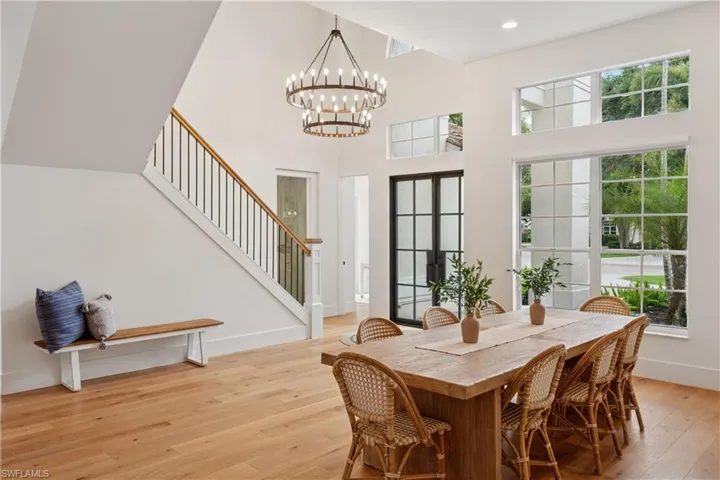 Dining room featuring stairway, light wood-style flooring, a chandelier, a towering ceiling, and baseboards