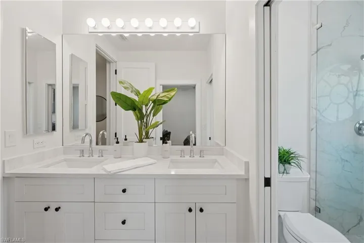 Bathroom featuring a marble finish shower, double vanity, and toilet