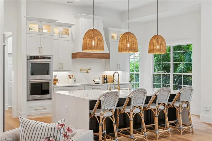 Kitchen with stainless steel double oven, a kitchen island with sink, tasteful backsplash, and light wood-type flooring