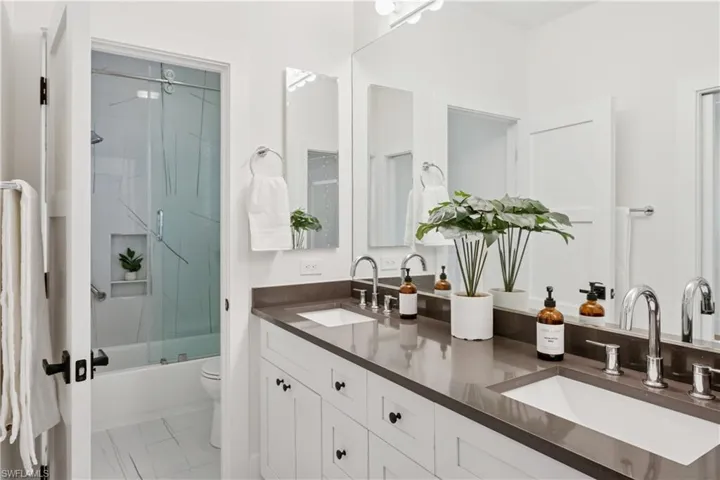Bathroom with double vanity, shower / bath combination with glass door, marble look tiles, and toilet