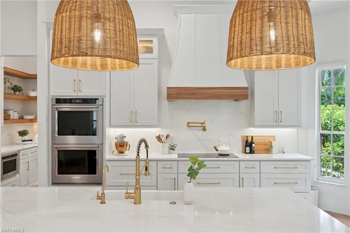 Kitchen with stainless steel double oven, black electric stovetop, premium range hood, tasteful backsplash, and light stone counters
