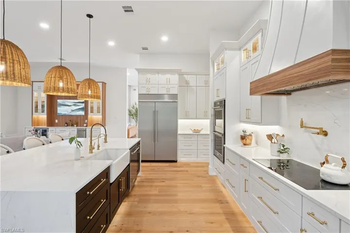 Kitchen featuring stainless steel appliances, premium range hood, a sink, light wood-style flooring, and white cabinetry