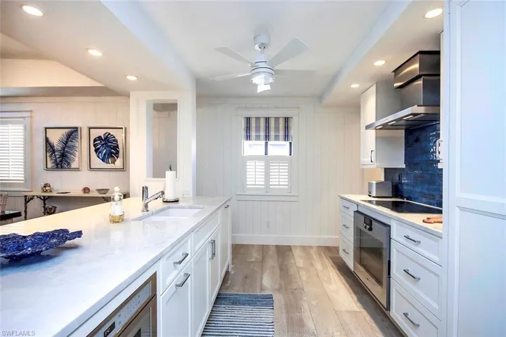 Kitchen featuring black electric stovetop, a sink, wall oven, wall chimney range hood, and light wood-type flooring
