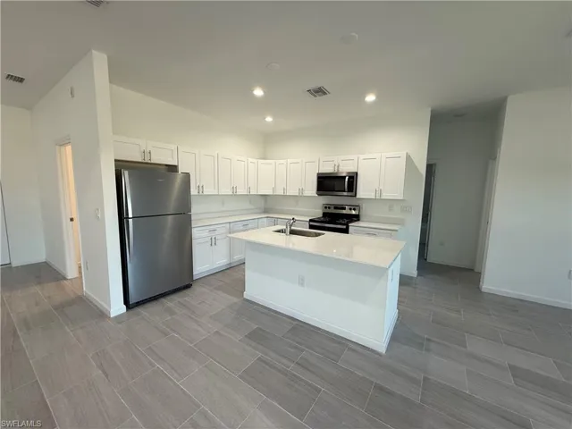 Kitchen with appliances with stainless steel finishes, white cabinets, a center island with sink, light stone counters, and recessed lighting