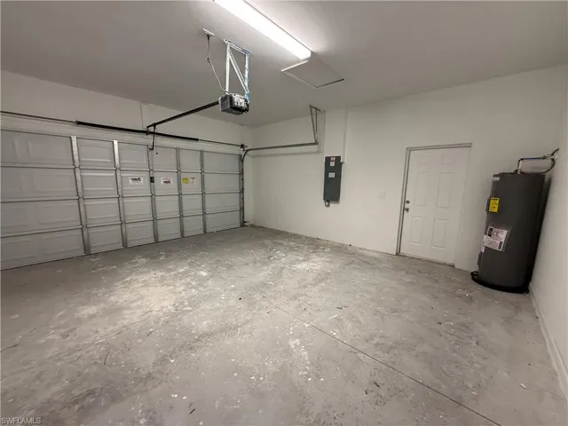 Garage featuring electric water heater, electric panel, and a garage door opener