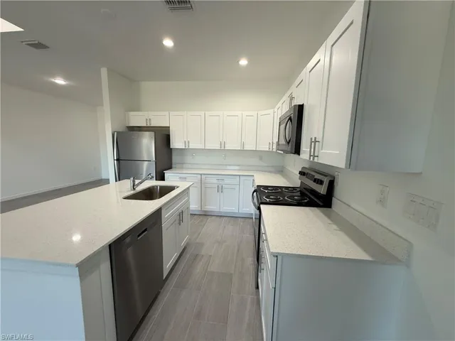 Kitchen featuring appliances with stainless steel finishes, white cabinets, an island with sink, light stone countertops, and recessed lighting