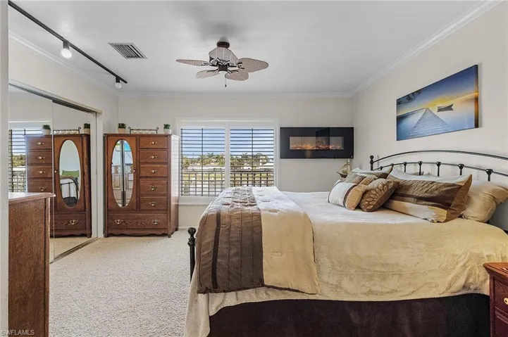 Bedroom featuring carpet flooring, track lighting, ceiling fan,crown molding, electric wall fire place