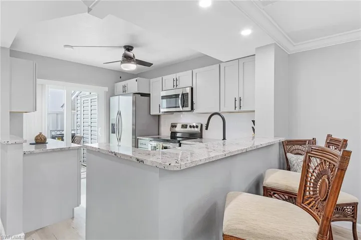 Kitchen with kitchen peninsula, backsplash, light wood-type flooring, appliances with stainless steel finishes, and a breakfast bar