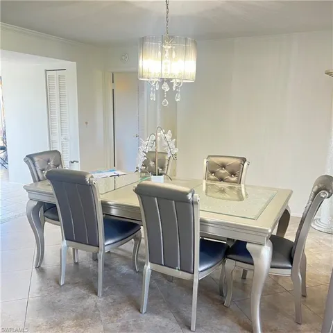 Dining room with light tile patterned floors, a chandelier, and crown molding