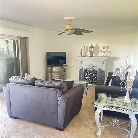 Living room with crown molding, a fireplace, light tile patterned floors, and ceiling fan