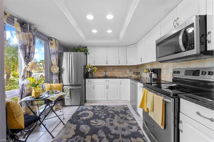 Kitchen featuring stainless steel appliances, a raised ceiling, white cabinetry, decorative backsplash, and recessed lighting