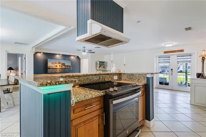 Kitchen with electric stove, wood finish cabinetry, light stone countertops, and ventilation hood