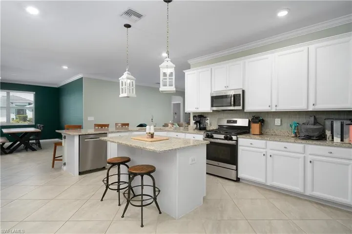Kitchen featuring a breakfast bar area, decorative light fixtures, a kitchen island, stainless steel appliances, and white cabinets