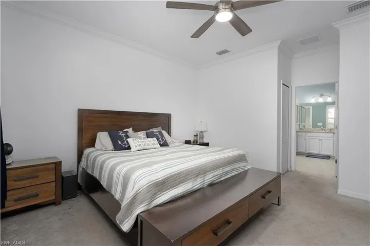 Bedroom featuring connected bathroom, crown molding, light colored carpet, and ceiling fan
