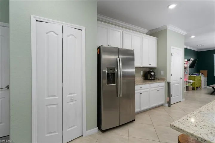 Kitchen with light stone counters, light tile patterned floors, ornamental molding, stainless steel fridge, and white cabinets